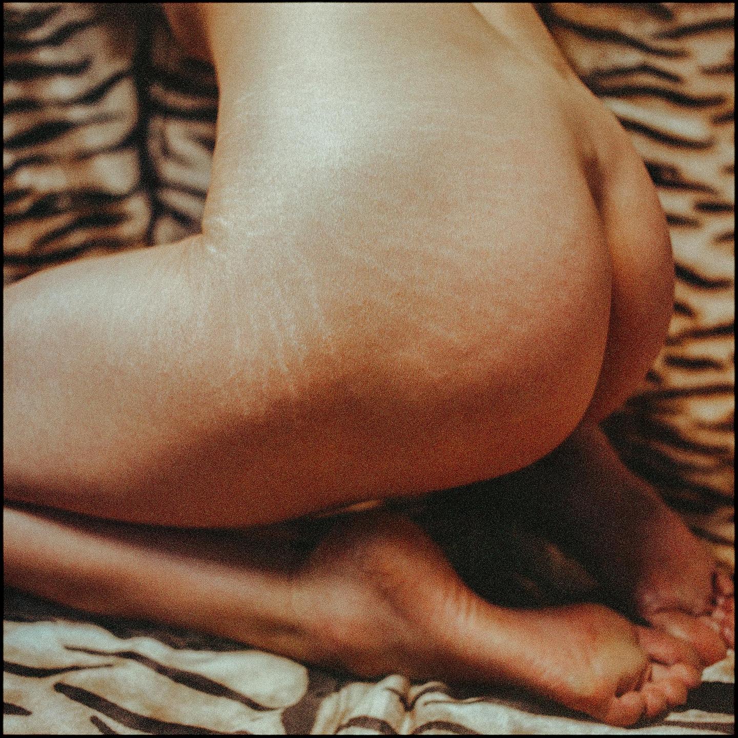 A person is kneeling on a tiger print blanket, showing their back, buttocks, and feet.