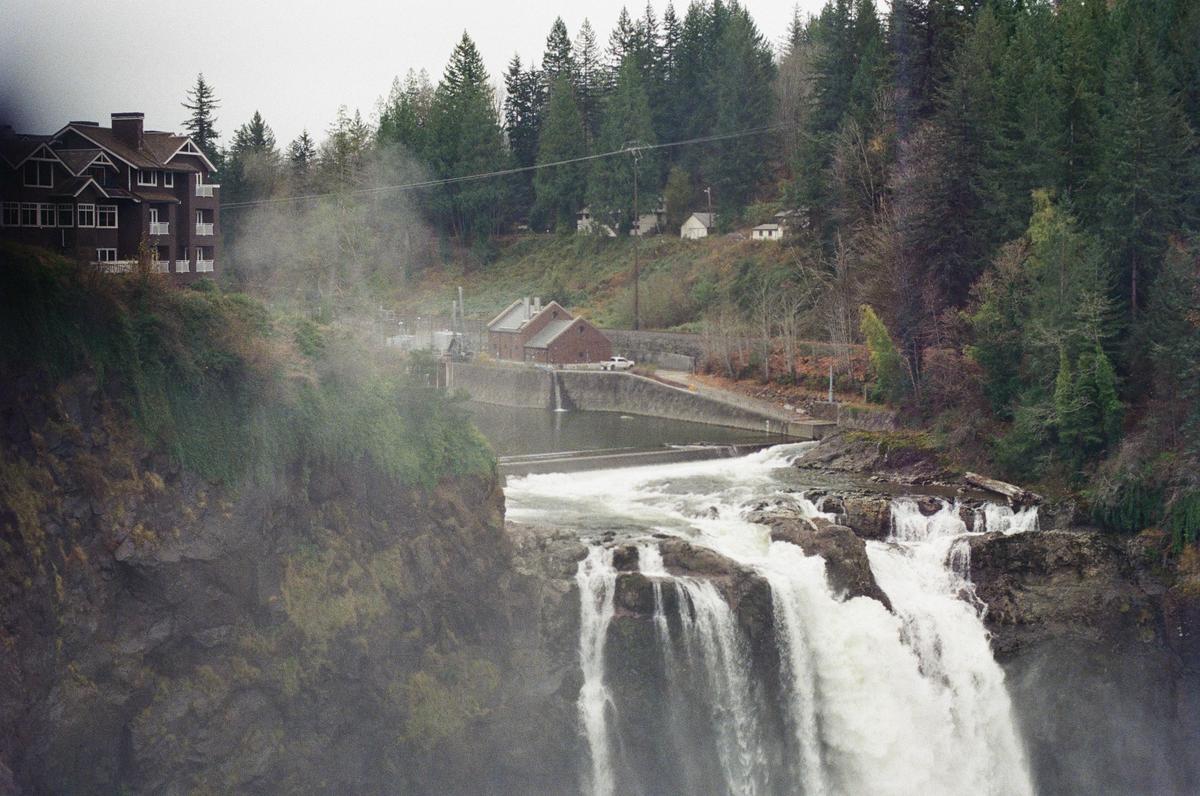 A large waterfall cascades over rocks with mist rising, and buildings are visible on the forested cliffs above.