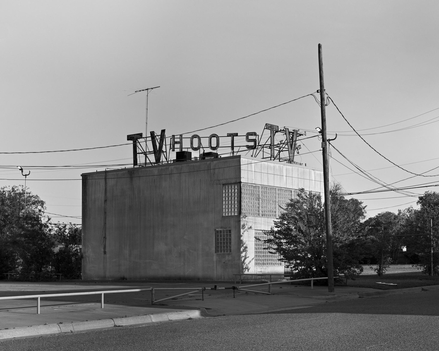 A building with a "Hoots TV" sign on its roof stands next to a utility pole with many wires.