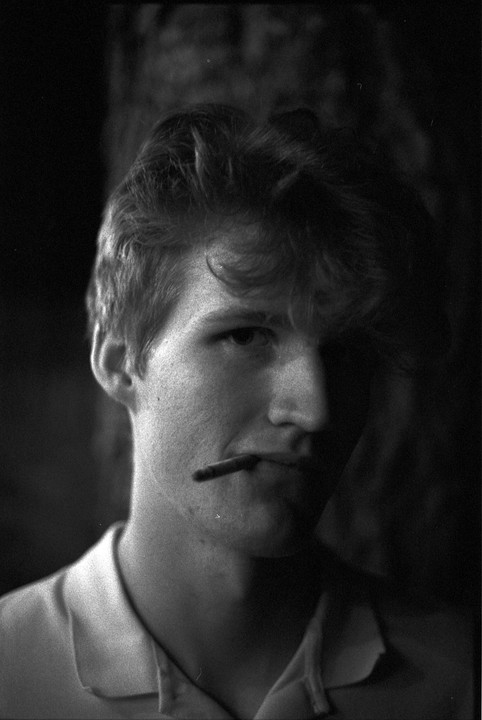 A man with a cigarette in his mouth looks towards the viewer.