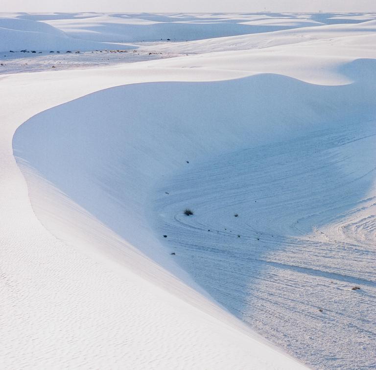 A vast desert landscape features white sand dunes under a clear sky.