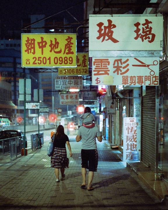 A family walks down a city street at night, passing storefronts with neon signs.
