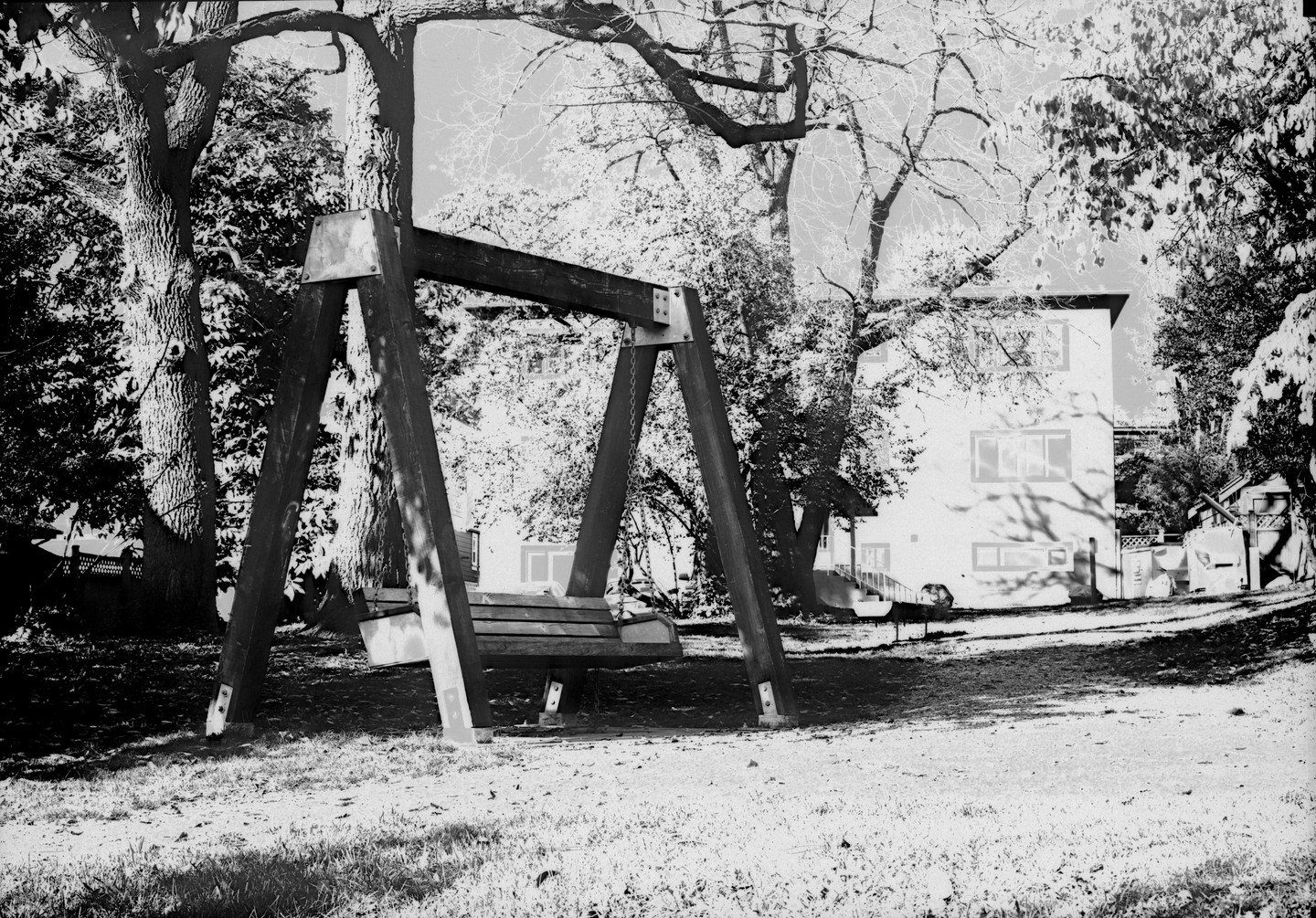 A wooden swing set sits in a grassy yard with a house and trees in the background.