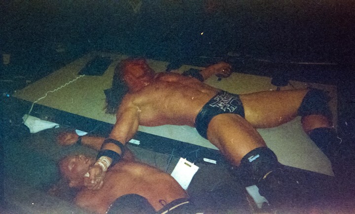 Two men are lying on the ground in a wrestling ring.
