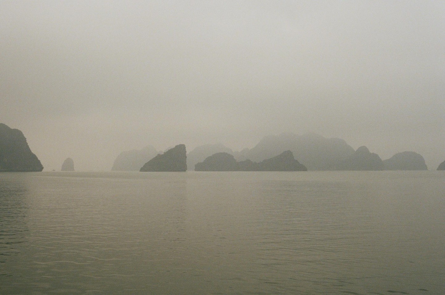 A body of water is surrounded by many small, rocky islands under a hazy sky.