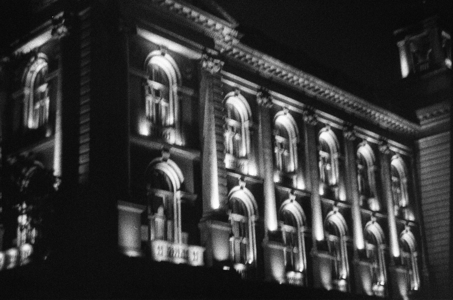 A building with many arched windows is illuminated at night.