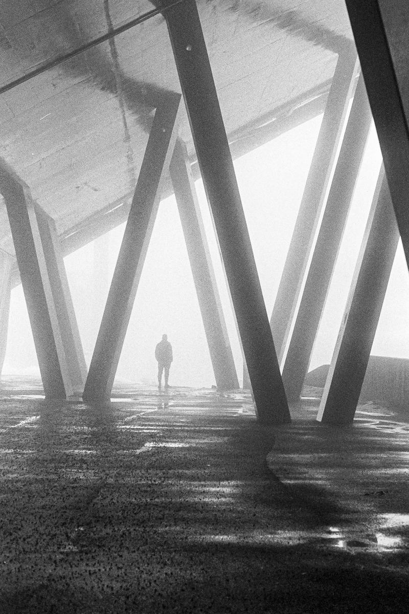 A person stands in a foggy, cavernous space with large, angled concrete pillars.
