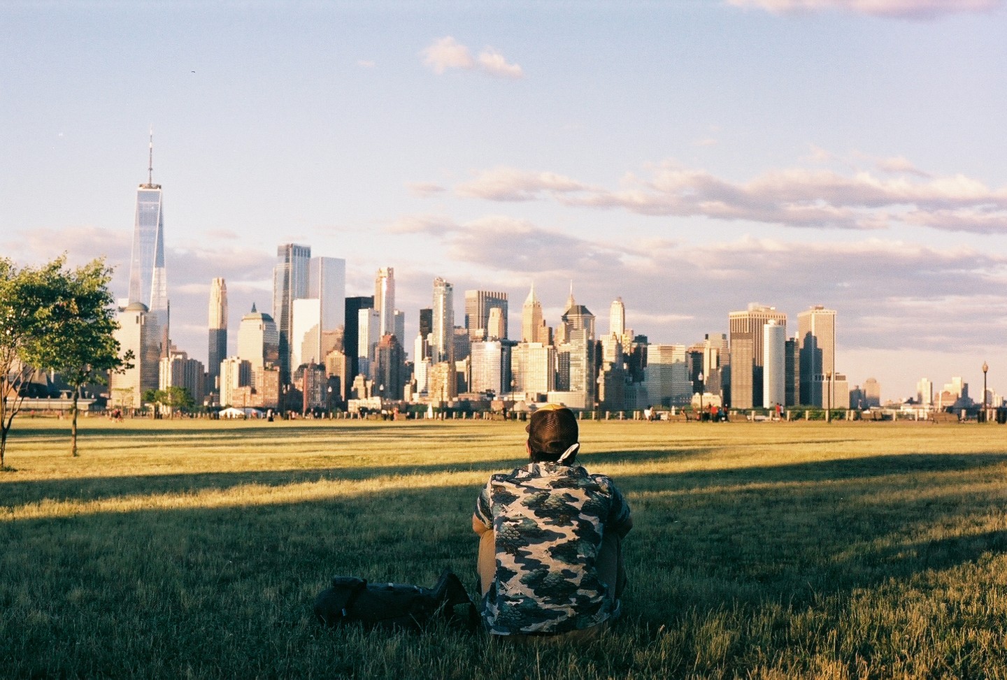 A man sits in a grassy field looking at the new york city skyline.