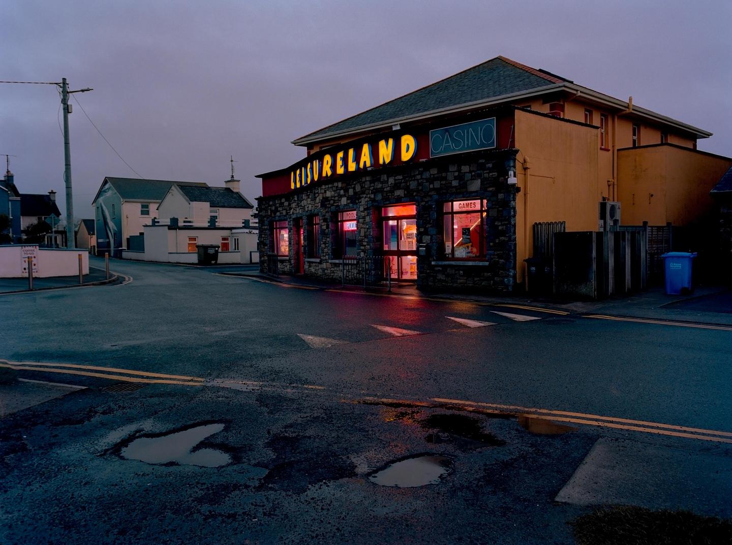 A street corner with a building featuring a "Leisureland Casino" sign illuminated at dusk.