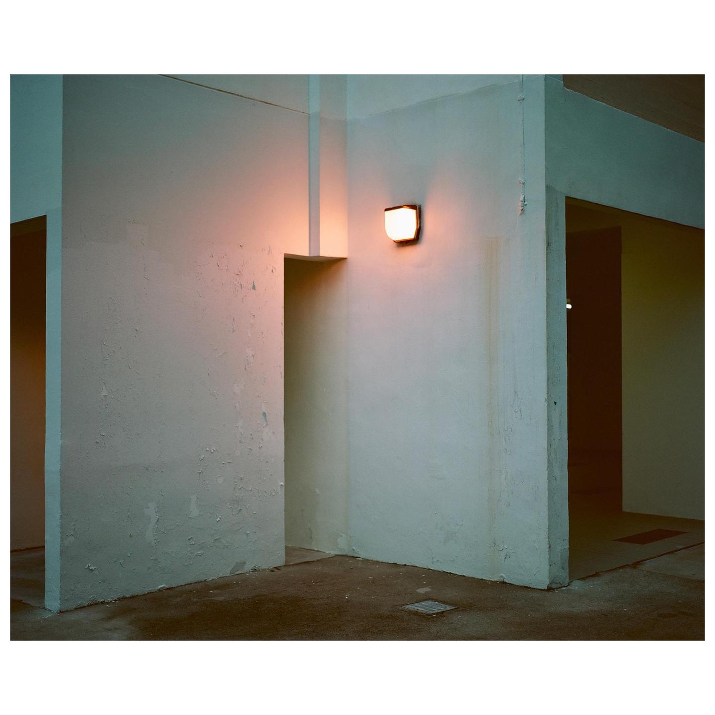 A single light illuminates a corner of a corridor with multiple doorways.