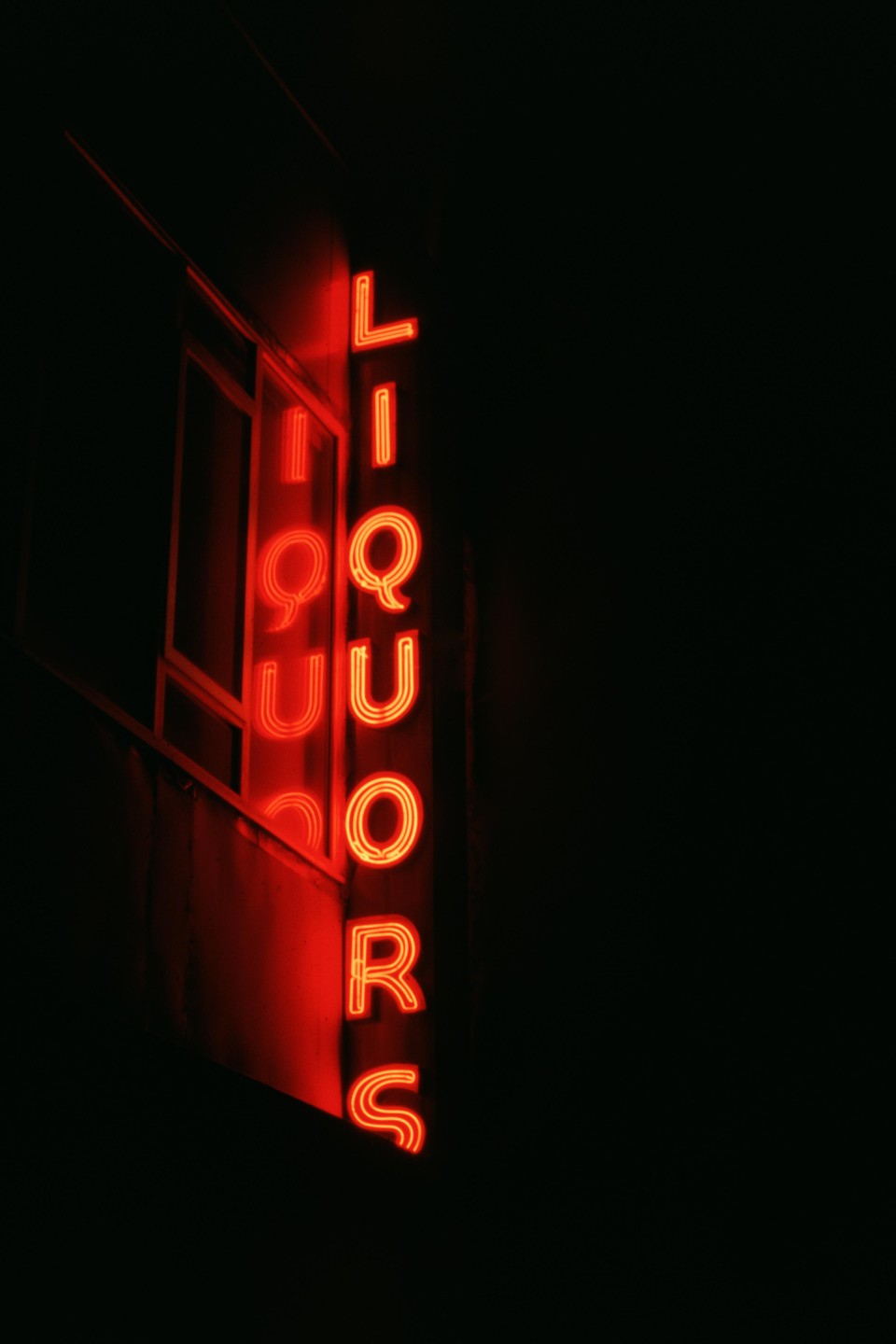 A red neon sign for "LIQUORS" is mounted vertically on the side of a building at night.
