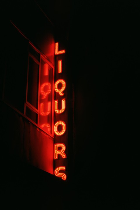 A red neon sign for "LIQUORS" is mounted vertically on the side of a building at night.