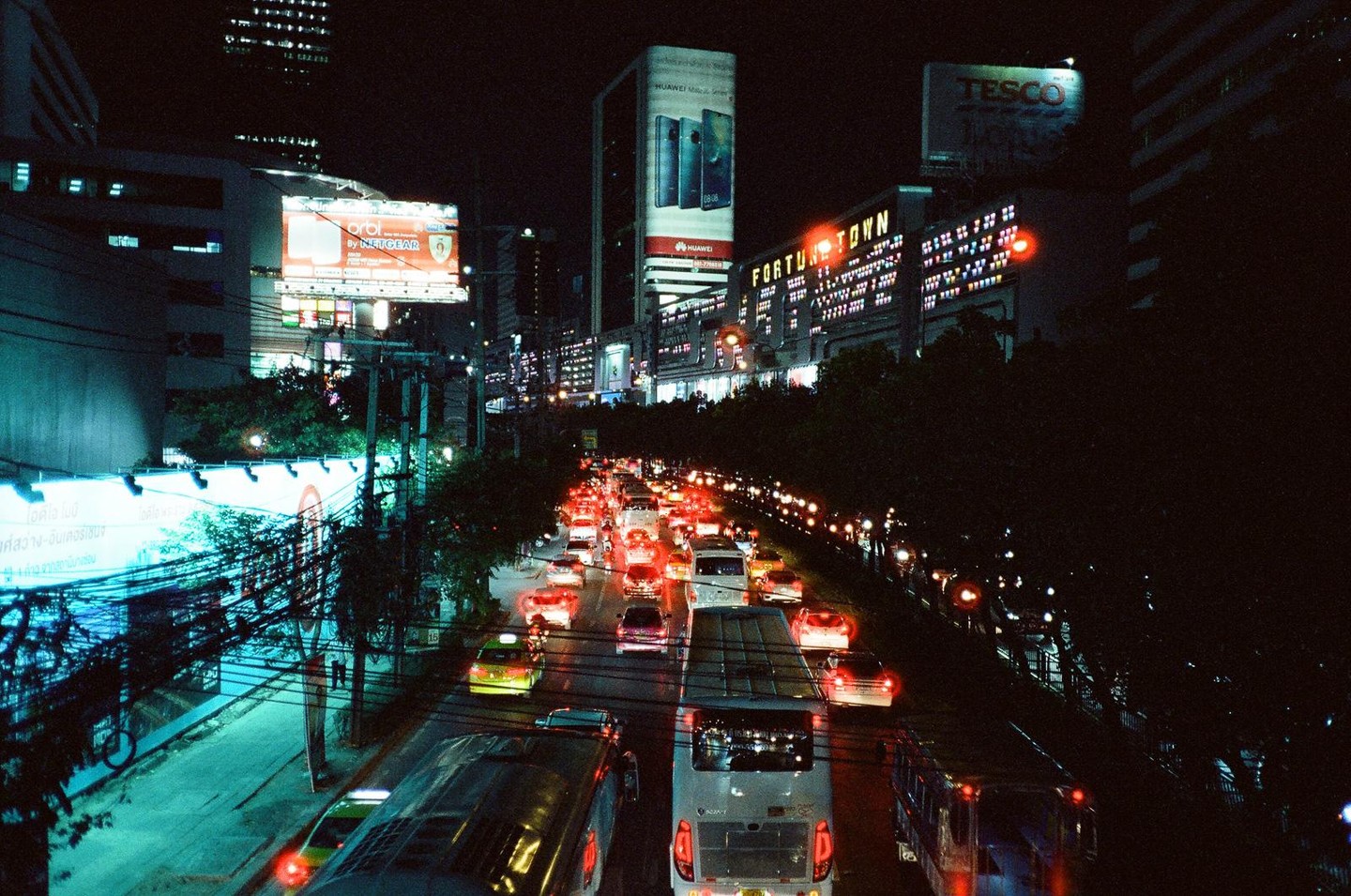 A busy street at night is filled with cars and buses, with illuminated buildings and billboards in the background.