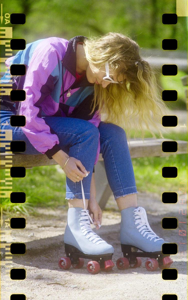 A woman wearing a colorful jacket and jeans sits on a bench, tying the laces of her roller skate.