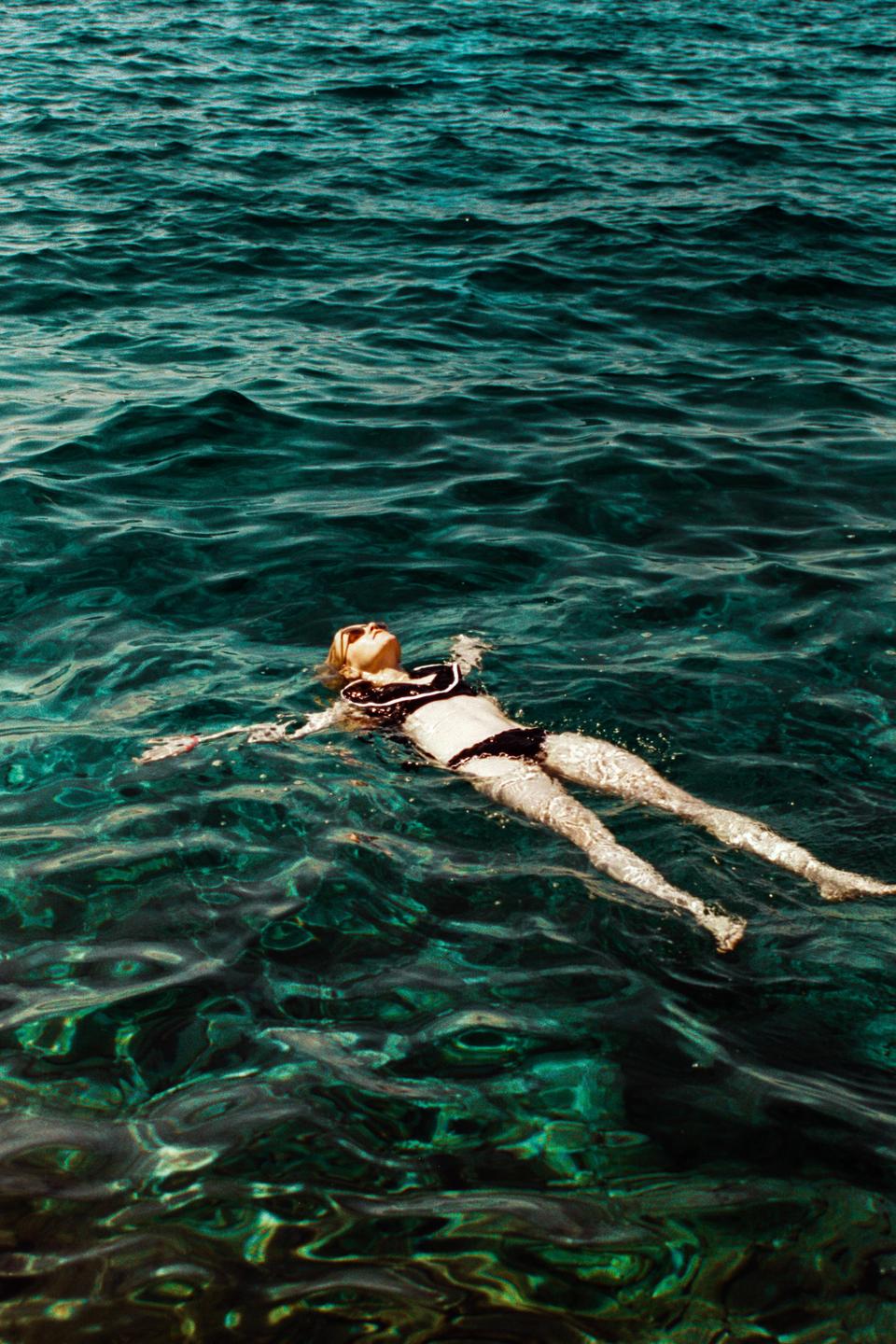 A woman floats on her back in clear blue-green water.
