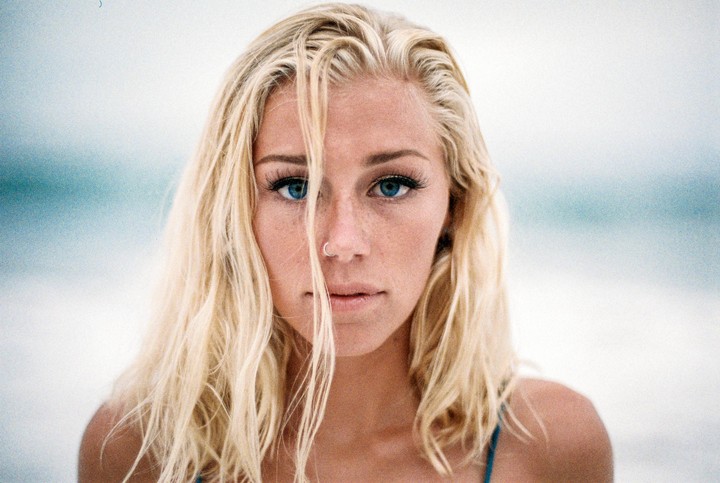 A woman with blonde hair and blue eyes looks directly at the viewer.