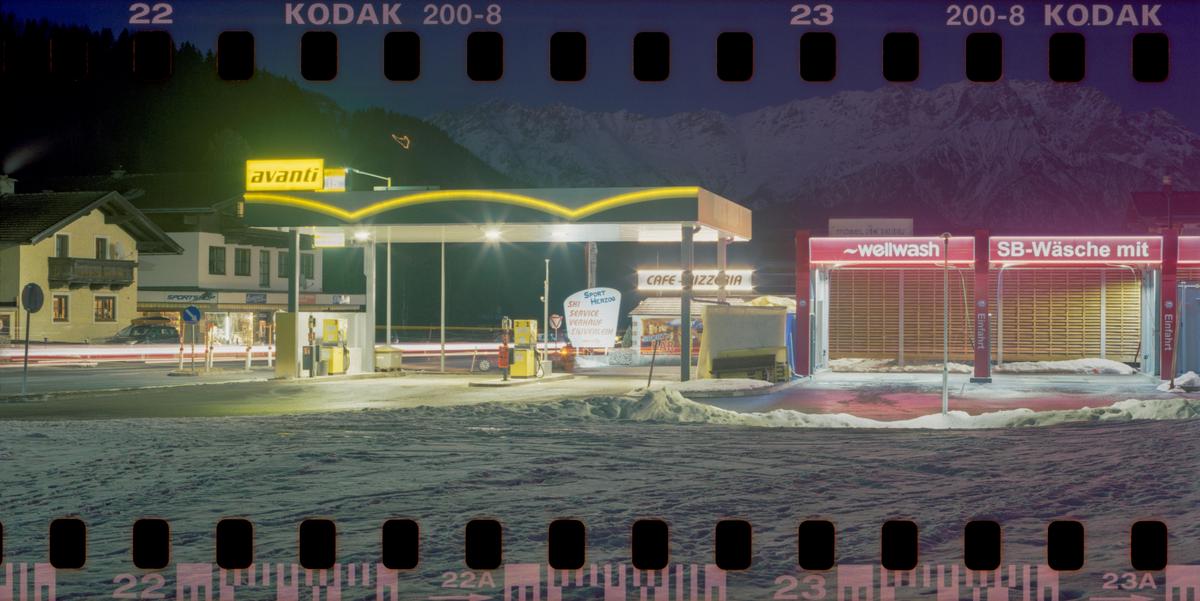A gas station and car wash are illuminated at night with mountains in the background.