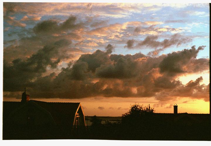 A dramatic sky with clouds at sunset is visible above the silhouette of a house and trees.