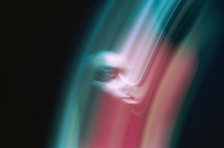 A blurry abstract image shows streaks of light in shades of pink, blue, and green against a dark background.
