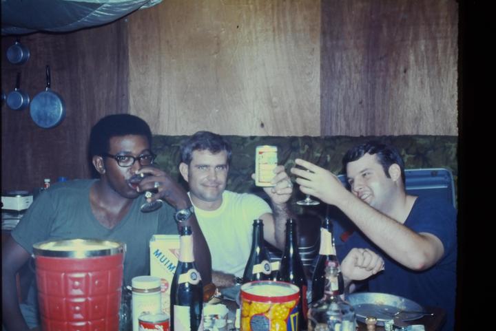 Three men are sitting around a table with drinks and bottles.