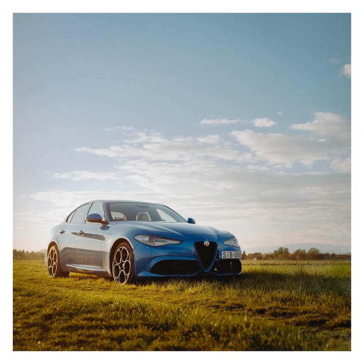 A blue car is parked in a grassy field under a partly cloudy sky.