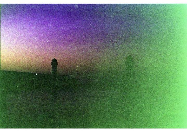 Two dark, silhouetted structures stand against a vibrant purple and green sky.