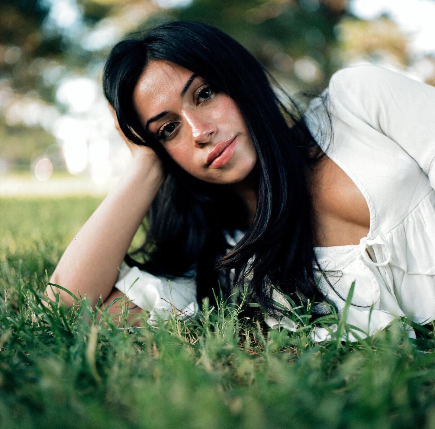 A woman with dark hair is lying on green grass, looking directly at the viewer.