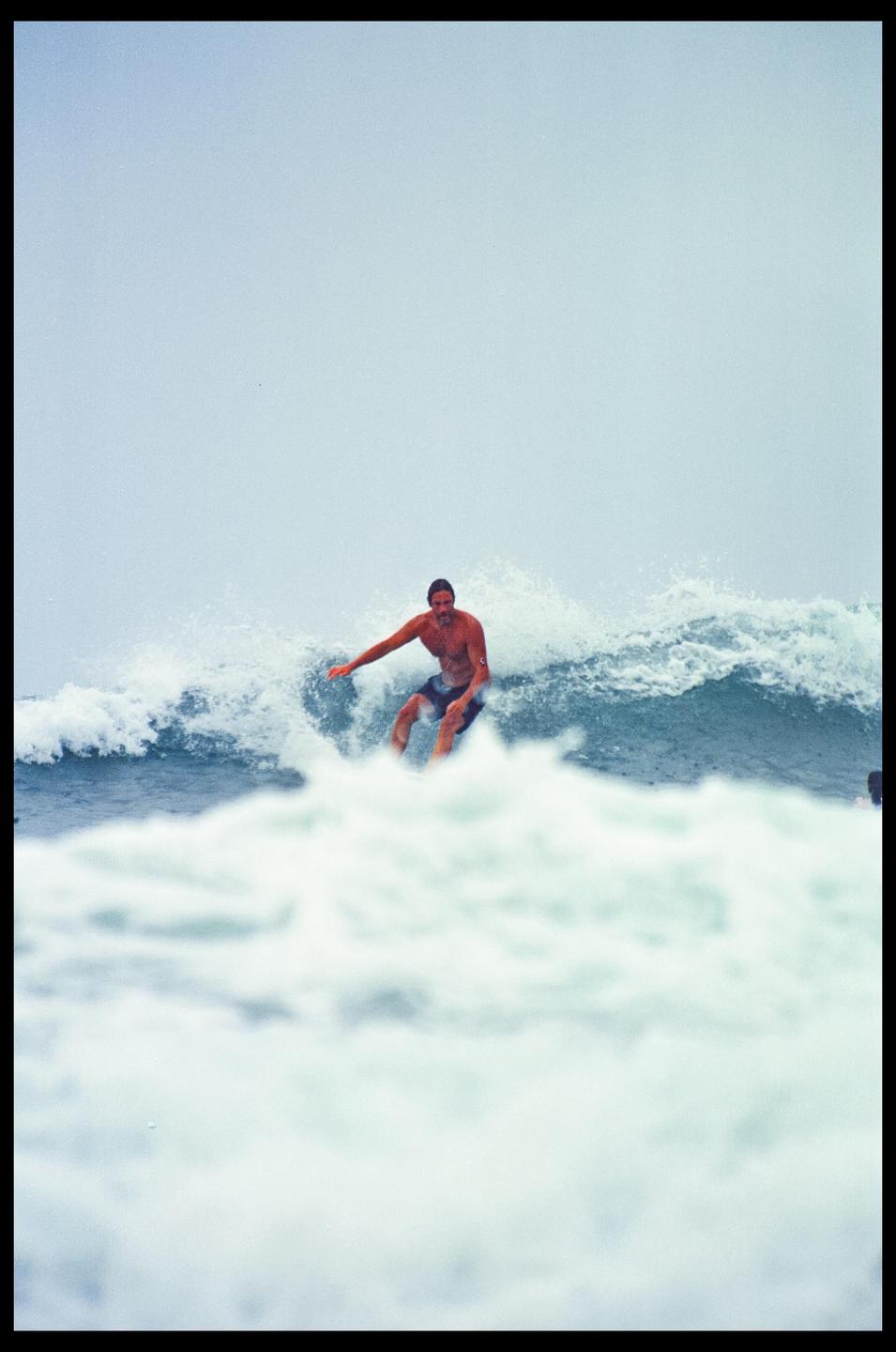 A man surfs a wave under an overcast sky.