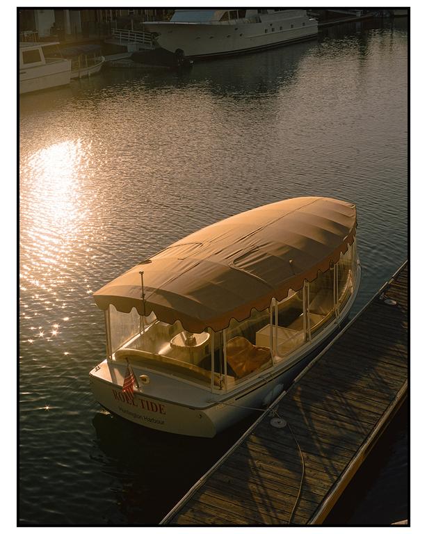 A small boat named Roll Tide is docked next to a wooden pier with sunlight reflecting on the water.