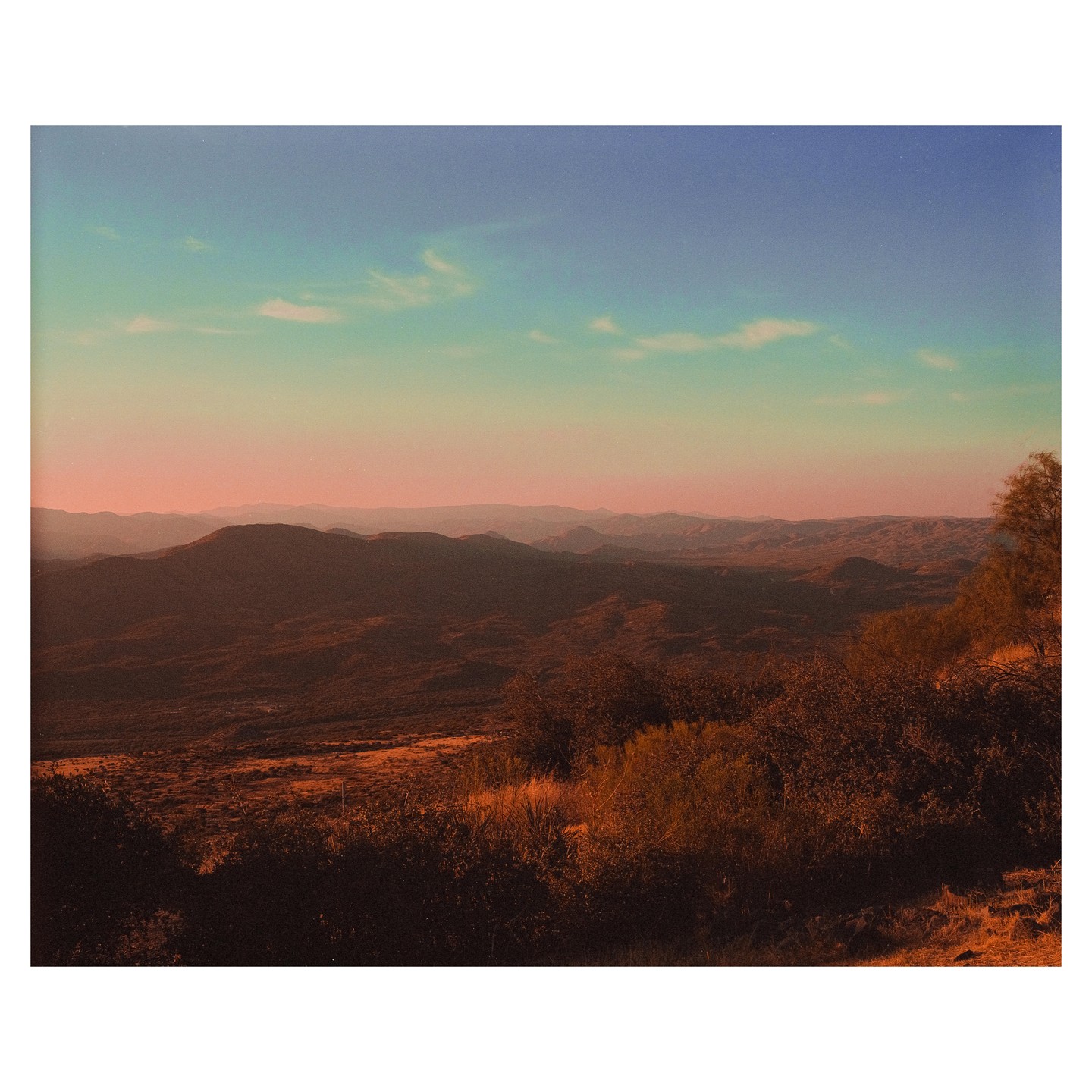 A vast desert landscape with mountains under a colorful sky is seen from a high vantage point.