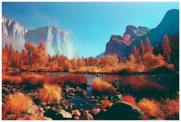 A river flows through a valley with orange trees and mountains under a blue sky.