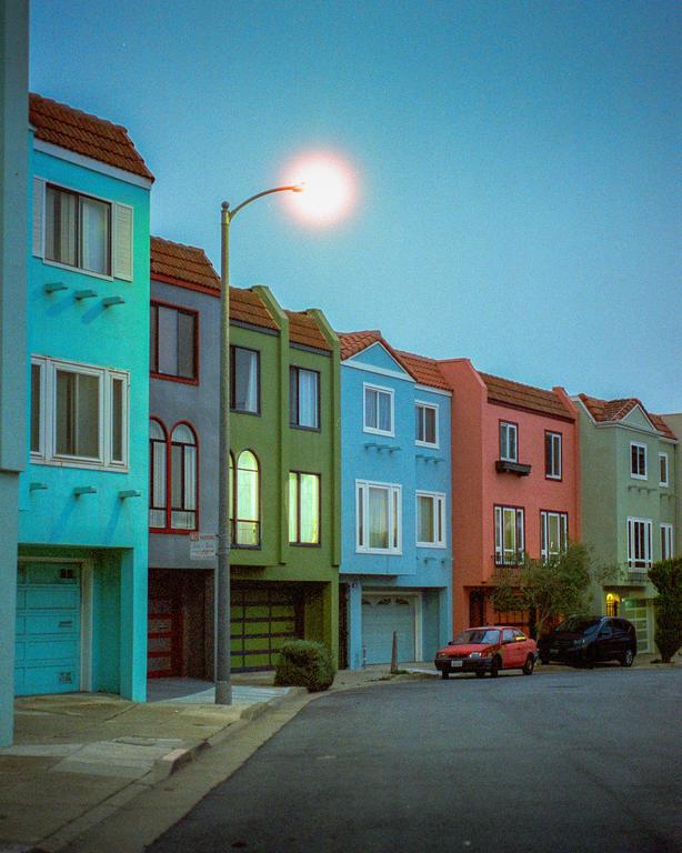 A row of colorful houses with cars parked on the street is illuminated by a street light.