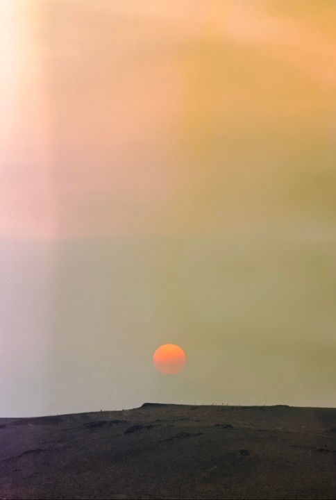 The sun sets over a desert landscape with a hazy sky.