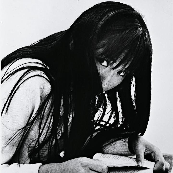 A woman with long dark hair looks up from a book she is reading.