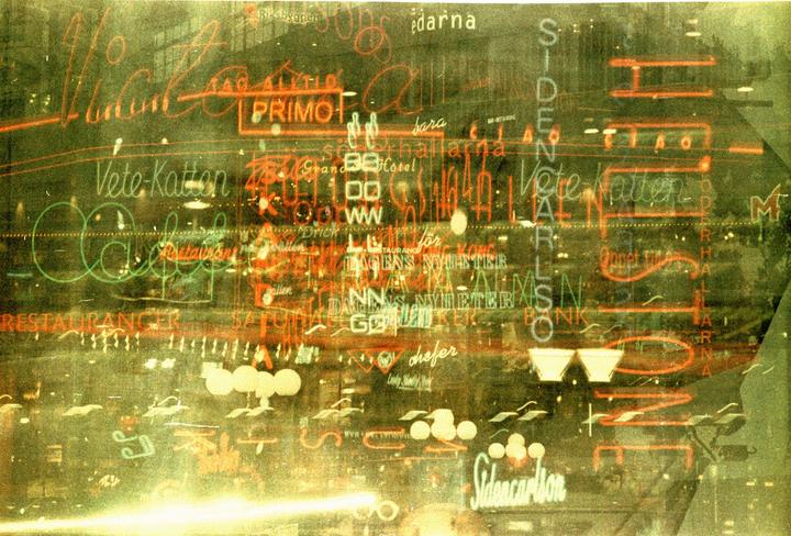 Multiple exposures of neon signs create an abstract pattern of light and text.