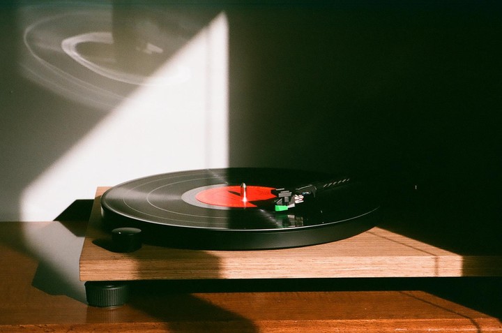 A record player with a red label record is bathed in a strong diagonal beam of sunlight.