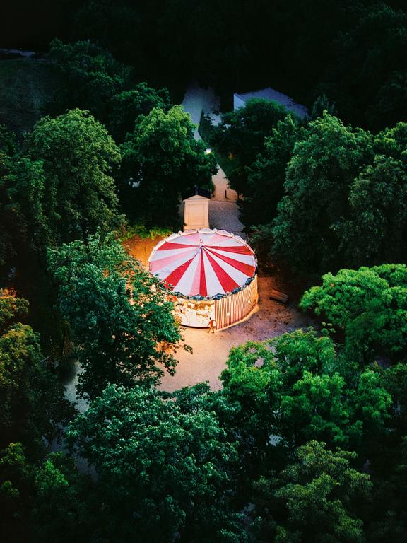 A red and white striped carousel is illuminated at night, surrounded by dark trees.