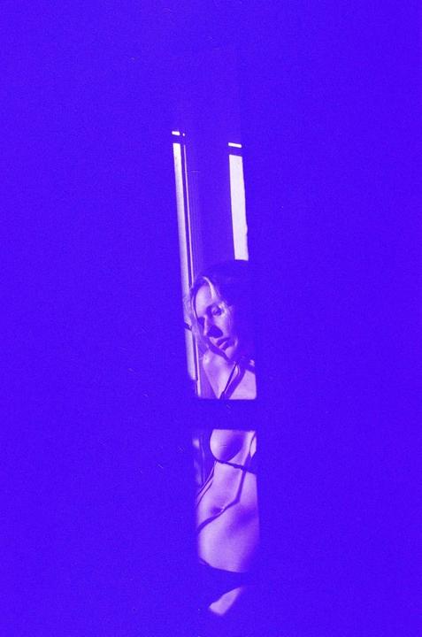 A woman is visible through a window with purple light and shadows.