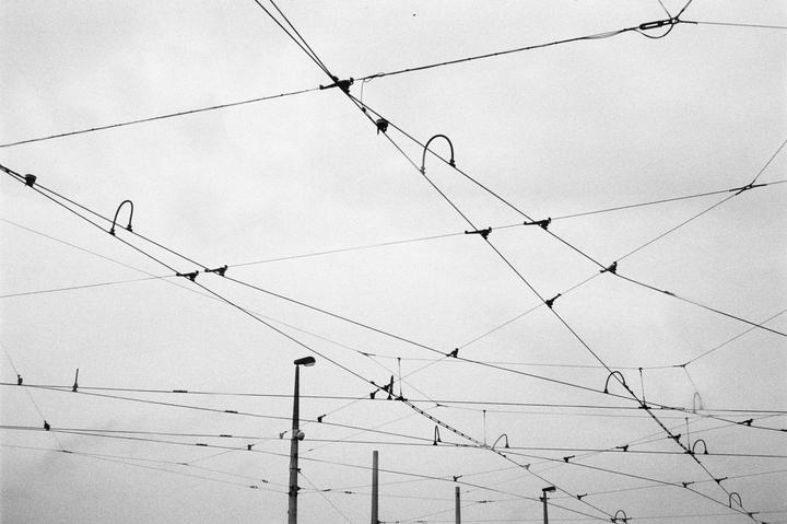 A complex network of overhead power lines and streetlights is visible against a bright sky.