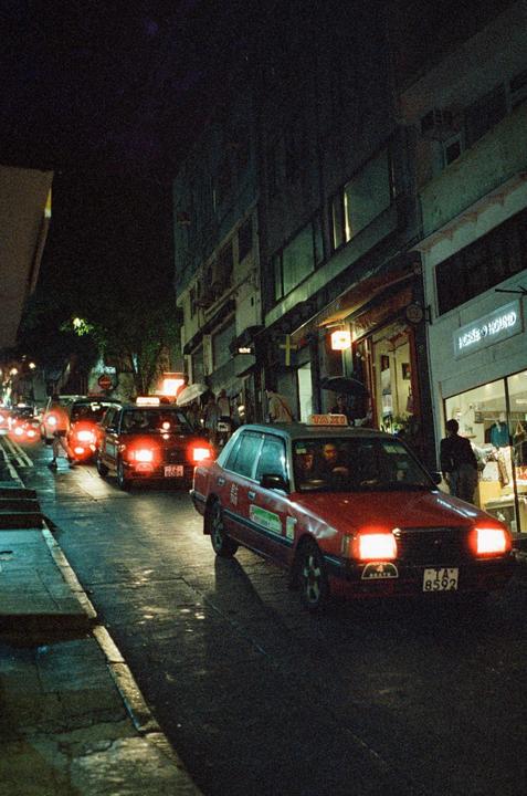 Red taxis drive down a wet street at night in Hong Kong.