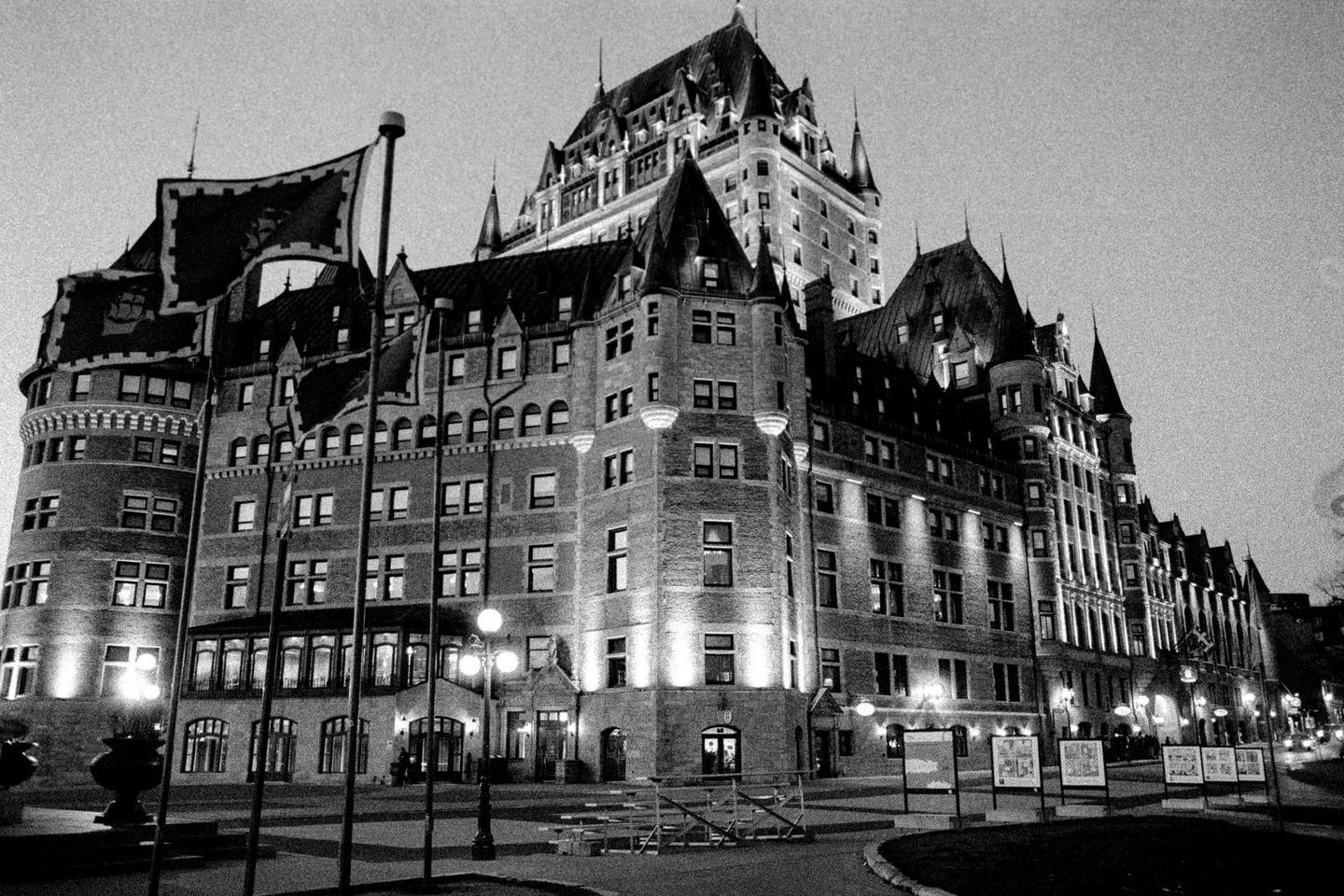 A large, ornate building with many turrets and flags is illuminated at night.