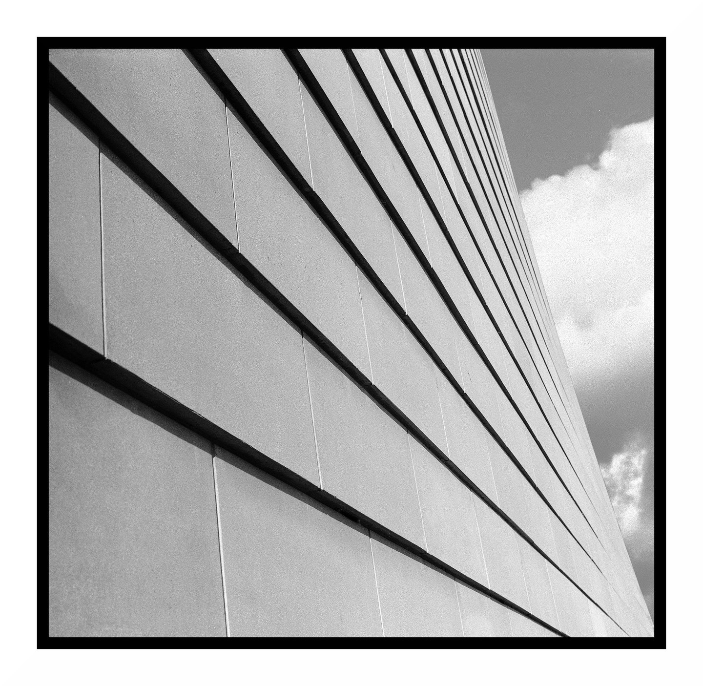 A low-angle view shows the side of a modern building with horizontal panels and a cloudy sky.