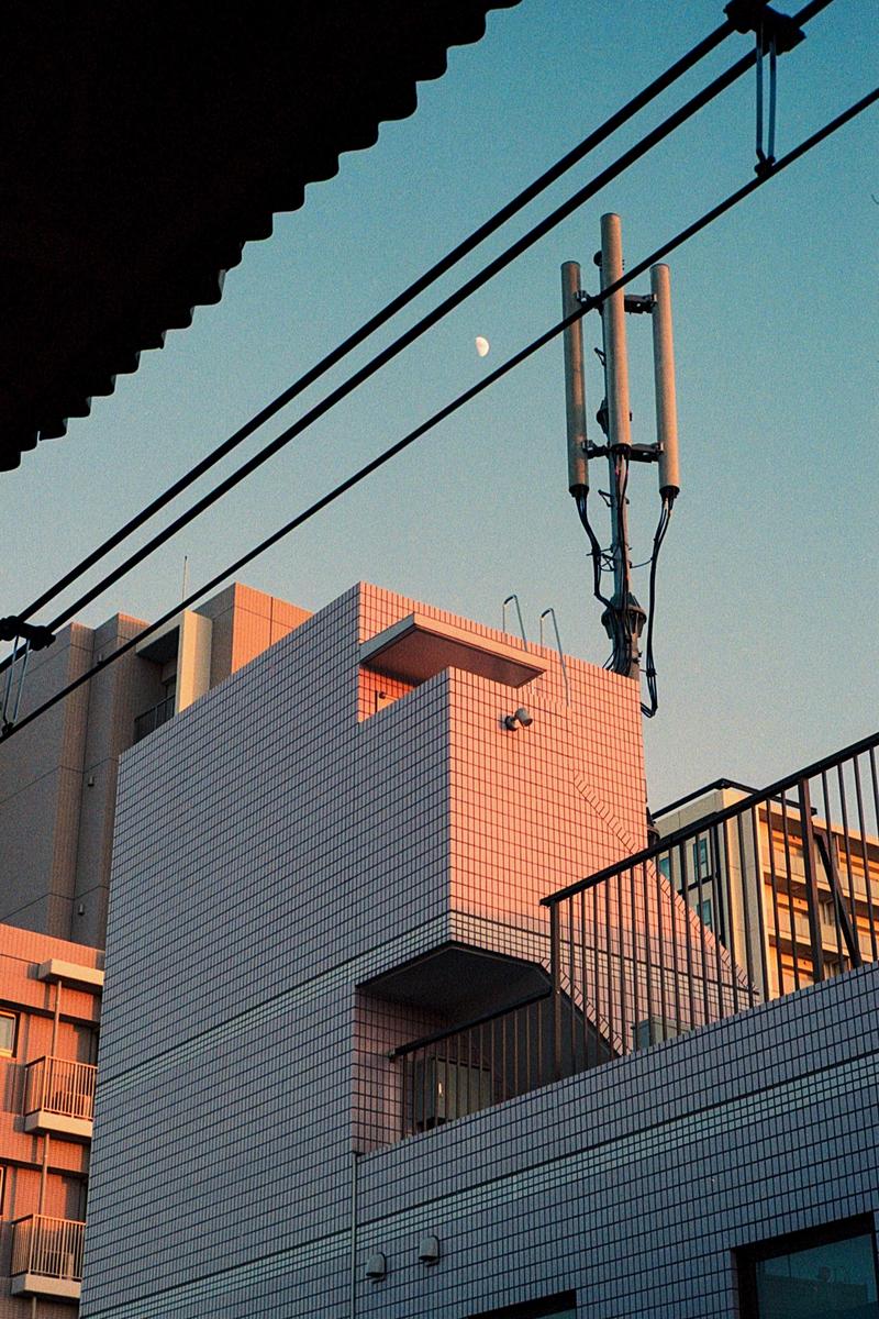 A crescent moon is visible in the sky above buildings and power lines.