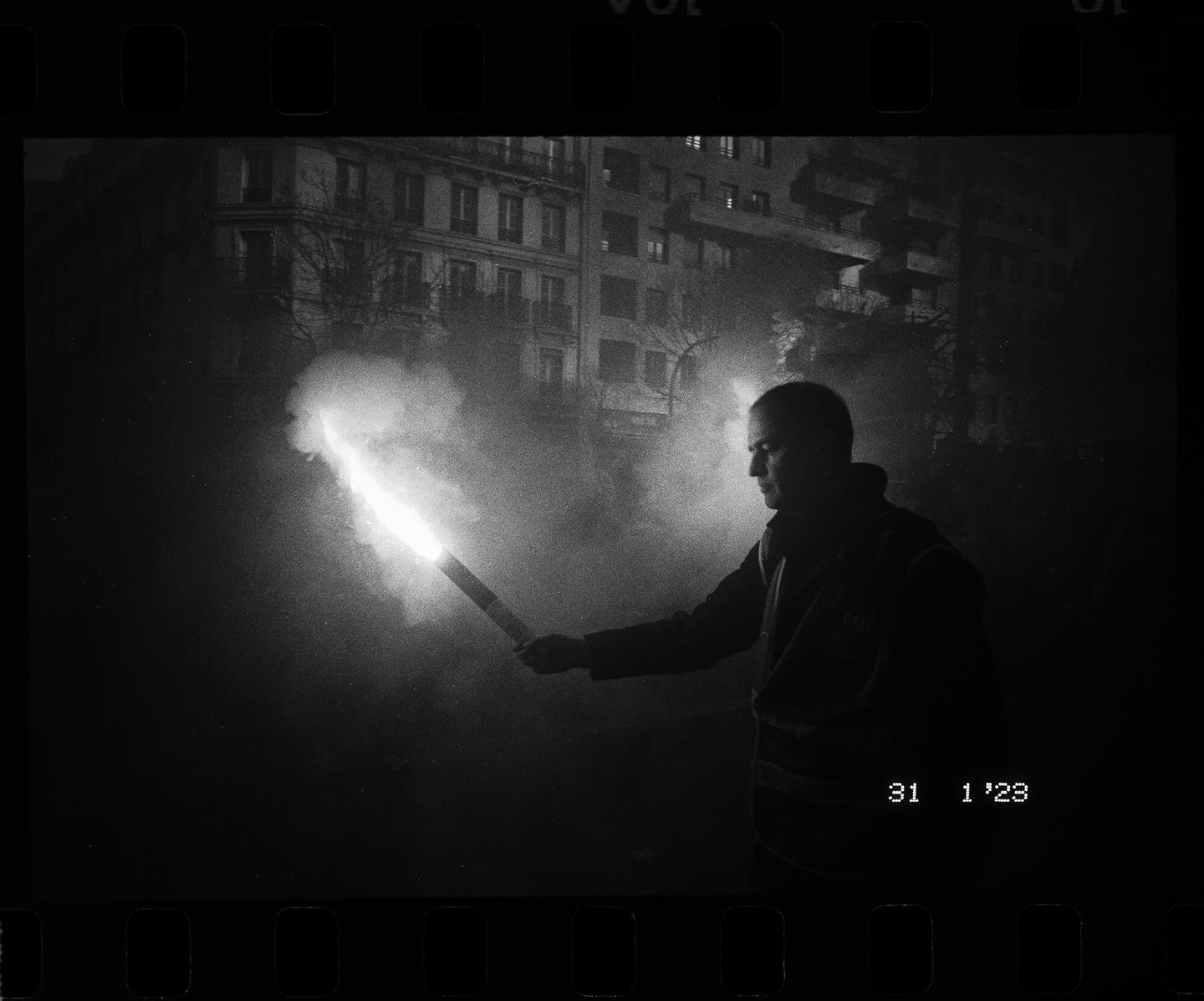 A man holds a flare that illuminates his face and the street at night.