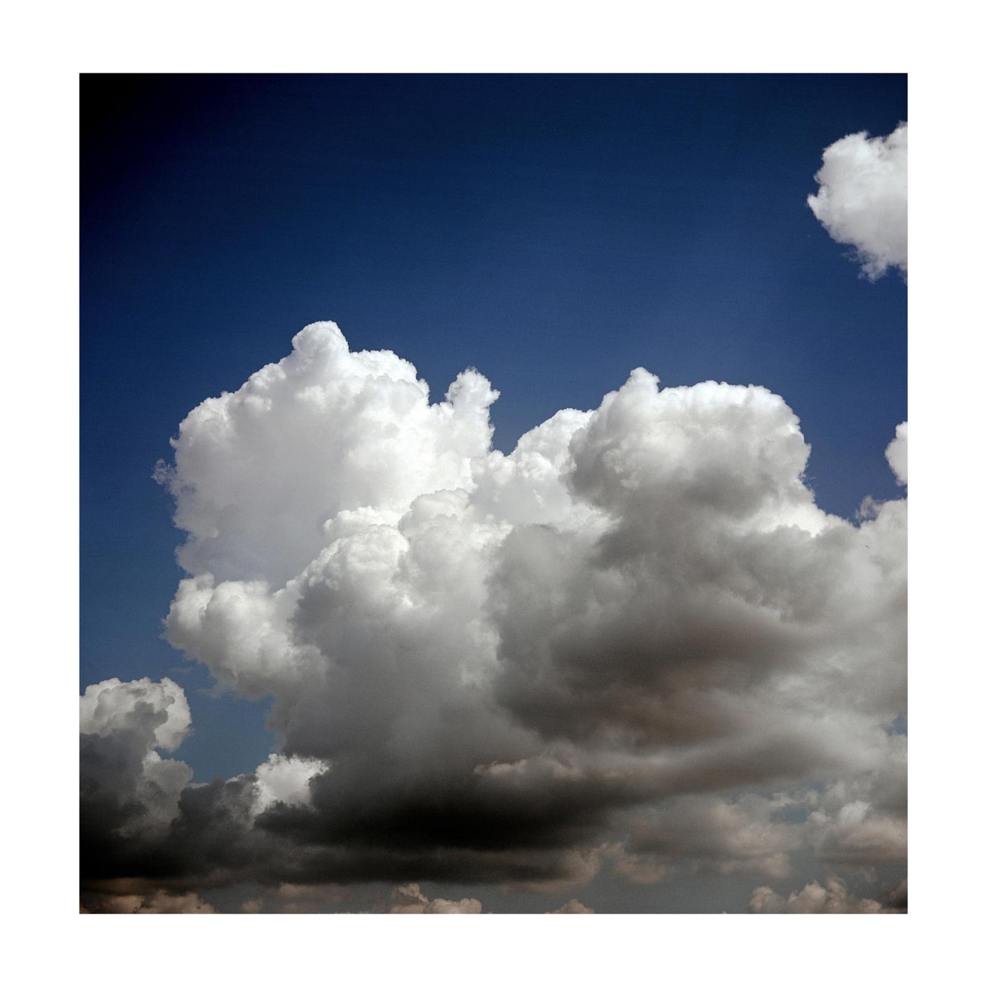 A large, fluffy white cloud is visible against a deep blue sky, with darker clouds below.