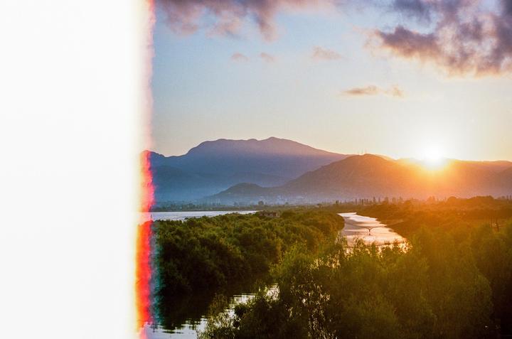 A river winds through a lush landscape with mountains in the background under a sunset sky.