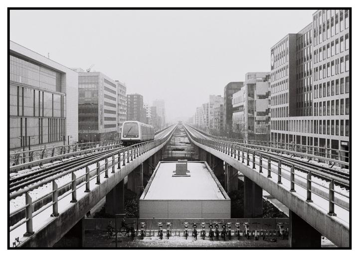 A metro train travels on an elevated track through a city covered in snow.