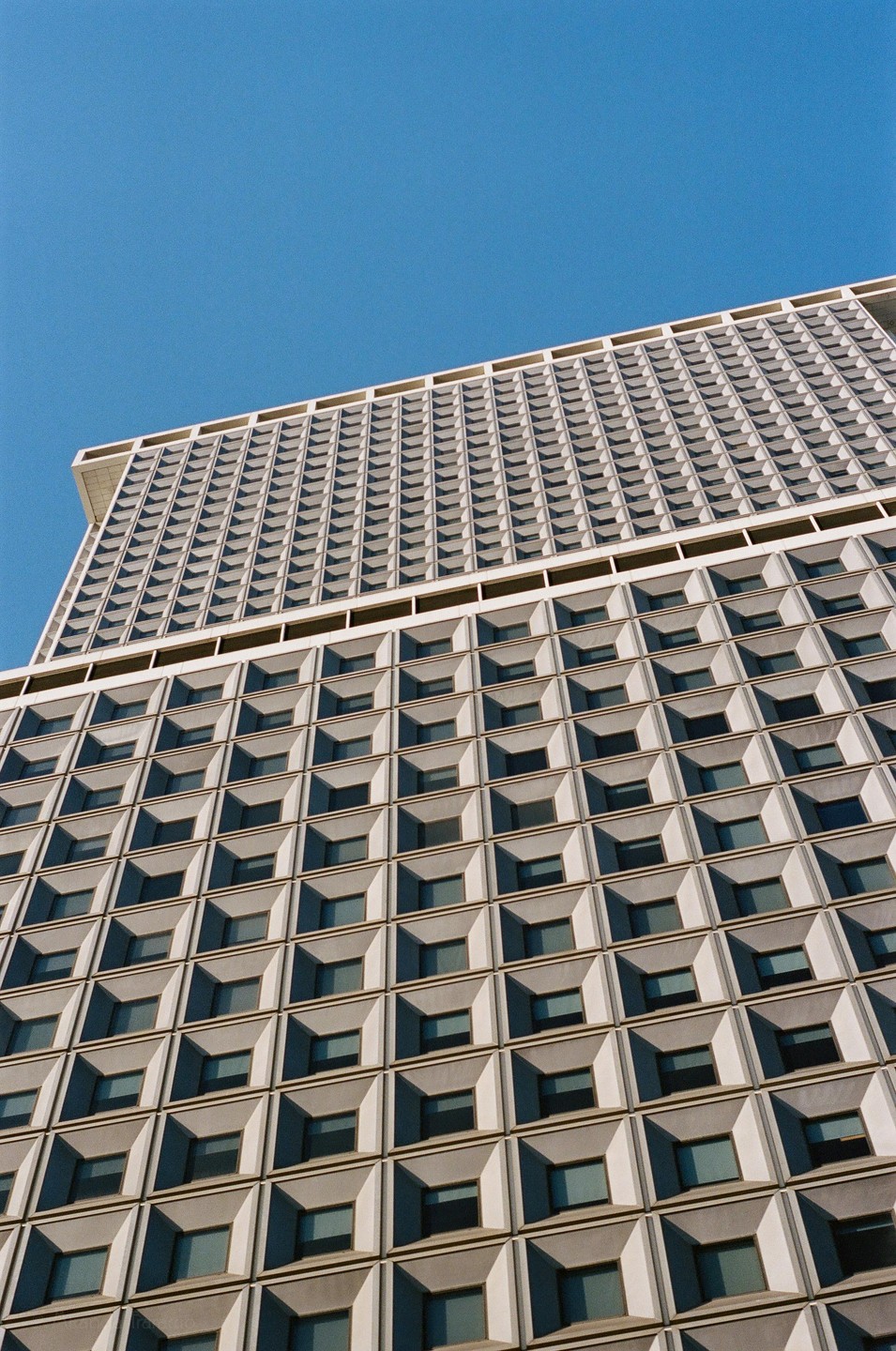 A tall building with a grid pattern of windows is shown against a clear blue sky.