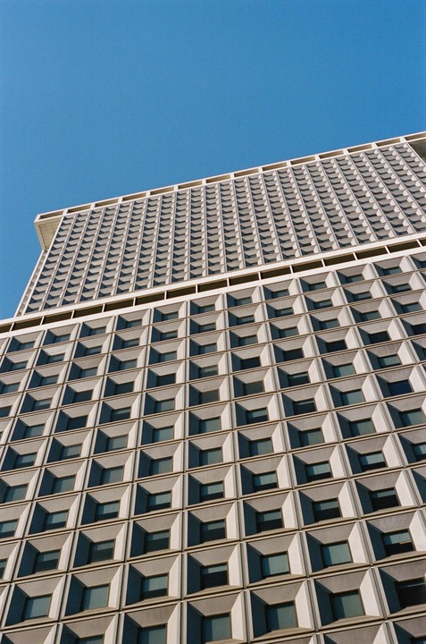 A tall building with a grid pattern of windows is shown against a clear blue sky.