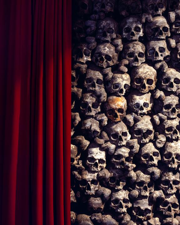 A red curtain hangs next to a wall made of human skulls and bones.